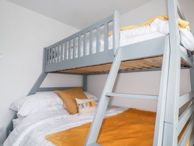 A bedroom with a grey bunk bed with white bedding and yellow blankets at Still Waters in Pentewan