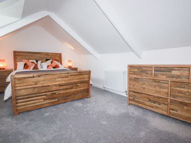 A bedroom with a wooden bed frame two bedside tables with lamps and a wooden dresser at Still Waters in Pentewan