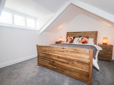 A bedroom with a wooden bed frame, two bedside tables with lamps, pillows on the bed and a window with shutters at Still Waters in Pentewan