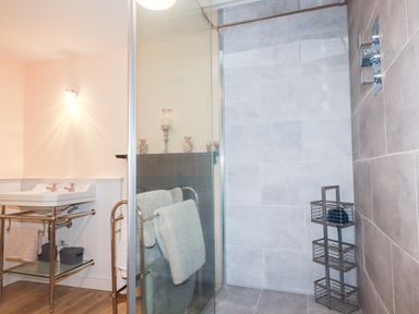 A bathroom with a glass shower enclosure a double sink with a metal stand and towels on a rack at Still Waters in Pentewan
