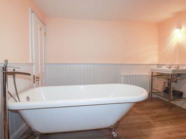 A bathroom with a freestanding bathtub a sink with dual taps a radiator and a wooden floor at Still Waters in Pentewan