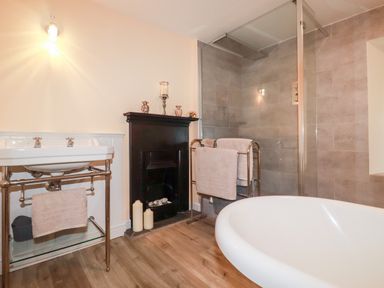 A bathroom with a freestanding bathtub sink with towels fireplace and glass shower at Still Waters in Pentewan