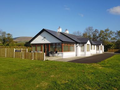 A single story white house with a dark roof and fenced patio on a lawn at Rose Cottage in Muff County Donegal
