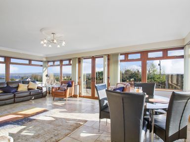 A living room with leather sofas chairs a dining table and large windows at Rose Cottage in Muff County Donegal