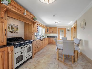 A kitchen with wooden cabinets a stove a dining table with chairs and tiled floor at Rose Cottage in Muff County Donegal