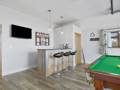 A recreation room with a bar counter and three stools a wall-mounted television and a pool table at Rose Cottage in Muff County Donegal