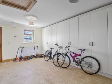 A storage room with bicycles and scooters lined up against a wall with white cabinets at Rose Cottage in Muff County Donegal