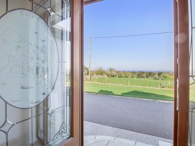 A view through a wooden door with decorative glass onto a road grass fields and trees at Rose Cottage in Muff County Donegal