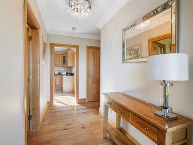 A hallway with wooden floor wooden doors a wooden table with a lamp and a mirror on the wall at Rose Cottage in Muff County Donegal
