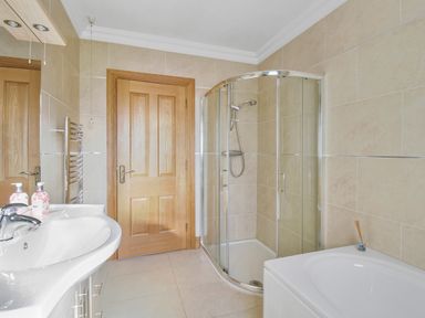 A bathroom with a wooden door a glass shower enclosure a white sink with soap dispensers and a bathtub at Rose Cottage in Muff County Donegal