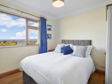 A bedroom with a bed and pillows next to a window with blue curtains at Rose Cottage in Muff County Donegal