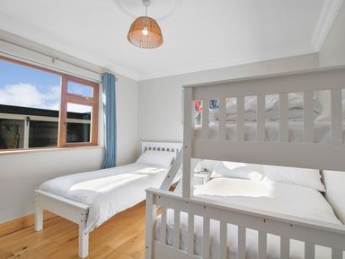 A bedroom with a single bed and a white bunk bed near a window with blue curtains at Rose Cottage in Muff County Donegal