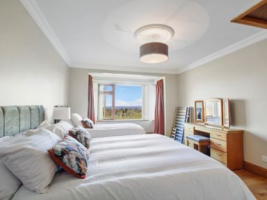 A bedroom with two beds a wooden dresser with mirrors and a window with curtains at Rose Cottage in Muff County Donegal