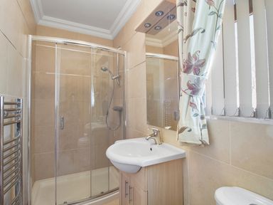 A bathroom with a glass shower enclosure sink with cabinet and a window with curtains at Rose Cottage in Muff County Donegal