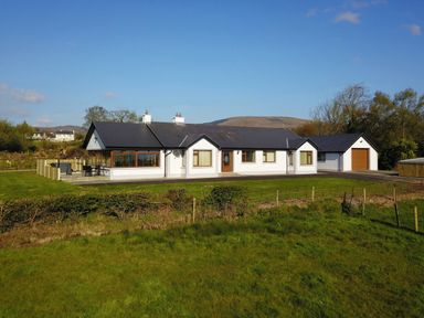 A single story house with white walls and a dark roof with an attached garage and lawn at Rose Cottage in Muff County Donegal