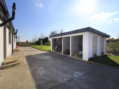 An outdoor area with a paved driveway a small building with open storage bays and grass at Rose Cottage in Muff County Donegal