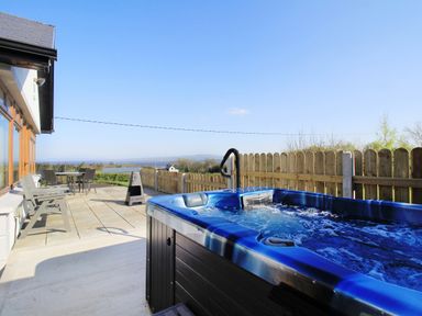 An outdoor patio with a hot tub wooden chairs a table and a fence in the background at Rose Cottage in Muff County Donegal