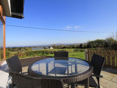 A glass topped round table with four wicker chairs on a patio overlooking fields and distant hills at Rose Cottage in Muff County Donegal