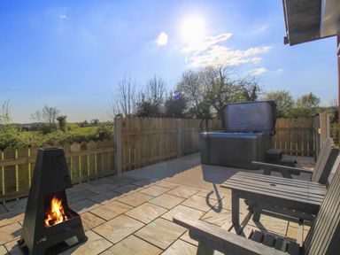 An outdoor patio with a fire pit wooden chairs and a hot tub with open cover at Rose Cottage in Muff County Donegal