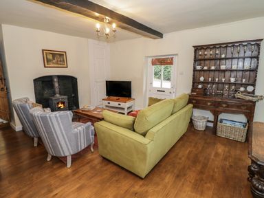 A living room with a wood burning stove two armchairs a green sofa a wooden cabinet and a television at Grove Cottage in Leominster