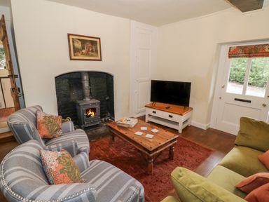 A living room with striped armchairs a green sofa a wooden coffee table a wood burning stove and a television at Grove Cottage in Leominster