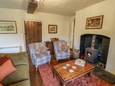A living room with two striped armchairs a green sofa a wooden coffee table and a wood burning stove at Grove Cottage in Leominster