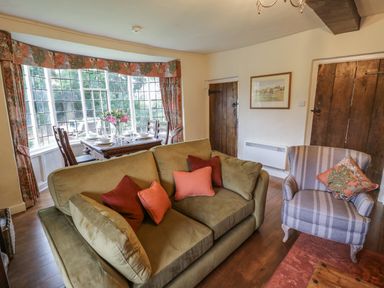 A living room with sofa and armchair next to a dining table by a window at Grove Cottage in Leominster