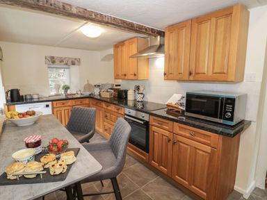 A kitchen with wooden cabinets a microwave oven and a table with scones and strawberries at Grove Cottage in Leominster