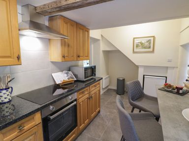 A kitchen with wooden cabinets a stove a microwave gray chairs and a small refrigerator at Grove Cottage in Leominster