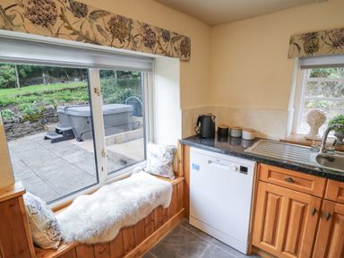 A kitchen corner with wooden cabinets a dishwasher a sink and a window seat with cushions at Grove Cottage in Leominster