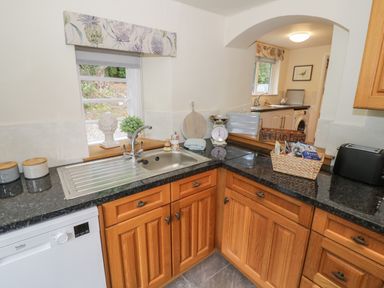 A kitchen with wooden cabinets a stainless steel sink a dishwasher and various kitchen items on the counter at Grove Cottage in Leominster
