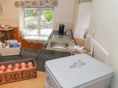 A kitchen with a sink a window seat with a cushion a basket of snacks and a wooden box of eggs at Grove Cottage in Leominster