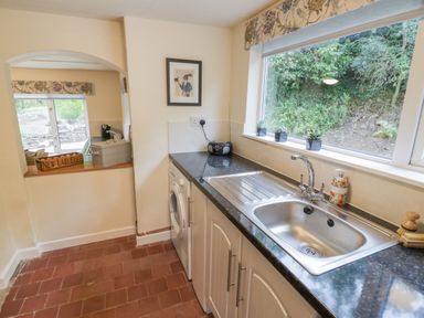 A kitchen with a sink washing machine radio and a window overlooking greenery at Grove Cottage in Leominster