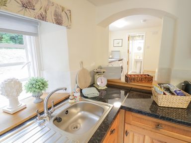 A kitchen counter with a sink and a window above it next to a cutting board a weighing scale and a crate of eggs at Grove Cottage in Leominster