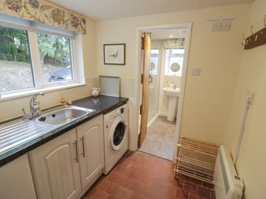 A utility room with a sink washing machine and a doorway leading to a bathroom at Grove Cottage in Leominster