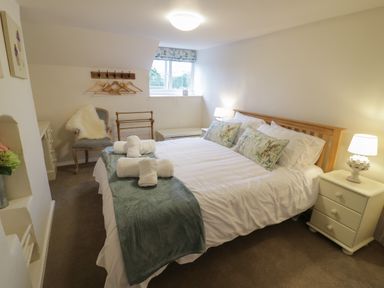 A bedroom with a made bed, bedside tables with lamps, a chair with a fur throw, and a window at Grove Cottage in Leominster