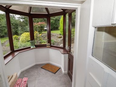 A small enclosed porch with tiled floor a doormat a wooden door and windows looking onto a garden at Grove Cottage in Leominster