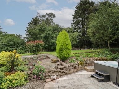 An outdoor garden area with stone retaining walls bushes and a hot tub with steps at Grove Cottage in Leominster
