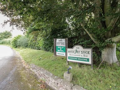 Two signs by a grassy roadside under a tree advertising The Hickory Stick Restaurant and Bar and golf and bowl activities at Grove Cottage in Leominster