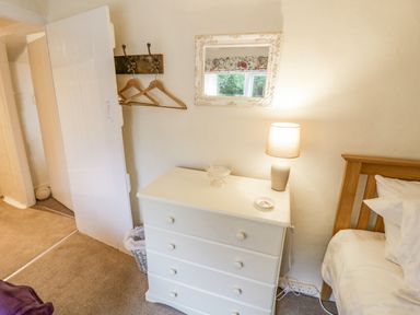 A bedroom with a white chest of drawers holding a lamp and dish next to a wooden bed at Grove Cottage in Leominster