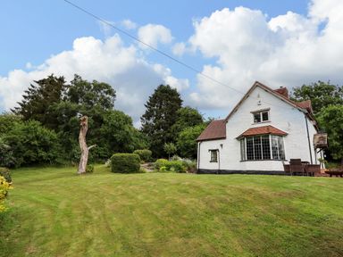 A white detached house with a lawn and trees at Grove Cottage in Leominster
