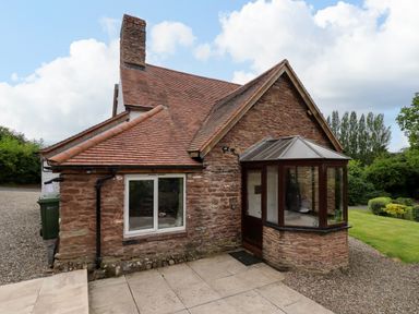 An exterior view of a stone cottage with a tiled roof and a small sunroom at Grove Cottage in Leominster