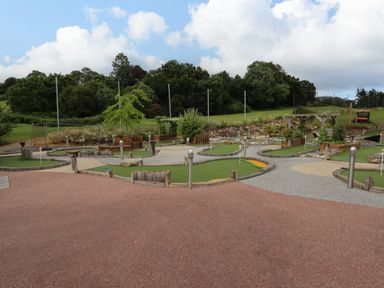 An outdoor mini golf course with multiple holes surrounded by grass trees and a wooden pergola at Grove Cottage in Leominster