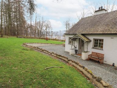 A cottage with a gravel path and wooden bench surrounded by grass and trees at Larch Cottage at Esthwaite Water in Hawkshead