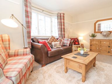A living room with a brown leather sofa and plaid armchair with a wooden coffee table at Larch Cottage at Esthwaite Water in Hawkshead