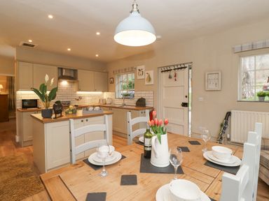 A kitchen and dining area with a wooden table set with plates glasses and a vase of tulips at Larch Cottage at Esthwaite Water in Hawkshead