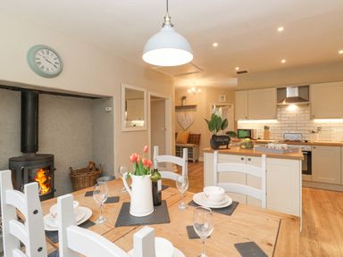 A kitchen and dining area with a wooden dining table set with plates and glasses a wood-burning stove and kitchen cabinets at Larch Cottage at Esthwaite Water in Hawkshead