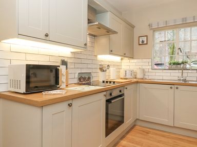 A kitchen with white cabinets wooden countertops a microwave and an oven below the stove with a window above the sink at Larch Cottage at Esthwaite Water in Hawkshead