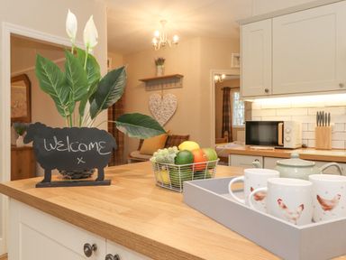 A kitchen countertop with a welcome sign, a plant, a fruit basket, and a tray with a teapot and mugs at Larch Cottage at Esthwaite Water Hawkshead