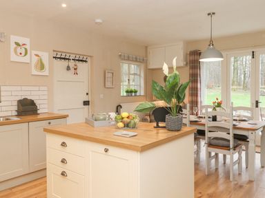 A kitchen with white cabinets a wooden island and a dining table with chairs by glass doors at Larch Cottage at Esthwaite Water in Hawkshead